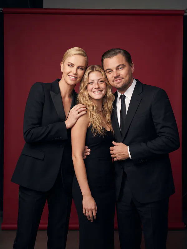 Retrato de família de estúdio de uma jovem loira com Charlize Theron e Leonardo DiCaprio num fundo vermelho