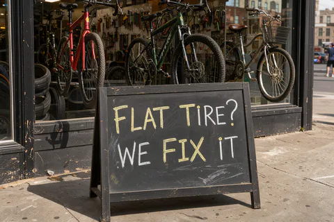 Um cavalete de lousa com a frase FLAT TIRE? WE FIX IT na frente de uma oficina de bicicletas