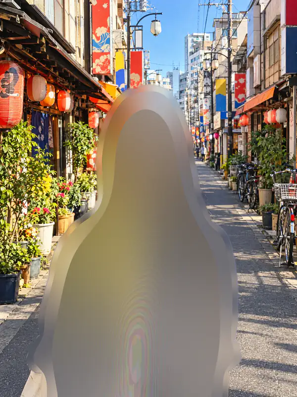下町の商店街を背景に、背景をぼかした青いシャツの女性。左上に元の写真