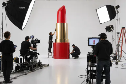 Um carro-conceito prateado num estúdio branco durante a gravação de um comercial, com softboxes e uma grua de câmera