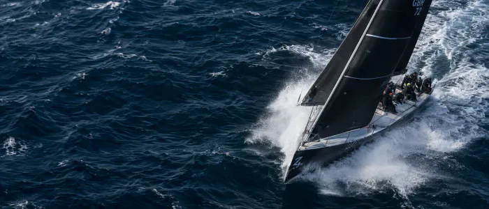 Um veleiro de regata inclinado cortando ondas azul-escuras, com borrifos no ar