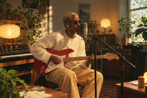 A singer with a red electric guitar recording in a cosy home studio